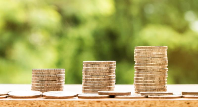 Three piles of coins in ascending levels of height, against a green background of what could be blurred leaves. 