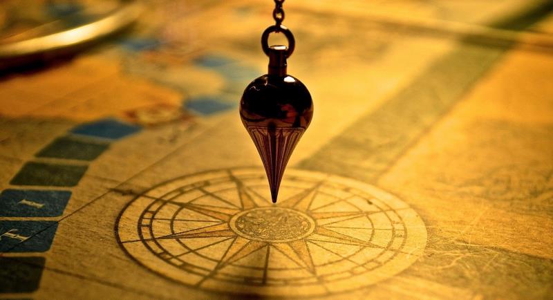 Photograph of a pendulum suspended over a vintage compass rose on an aged map, illustrating themes of navigation and direction. Warm lighting highlights intricate details of the compass and pendulum, emphasising exploration and decision-making concepts.